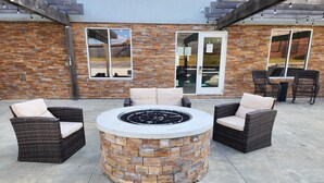 A patio area with a stone fire pit surrounded by wicker chairs and a table.