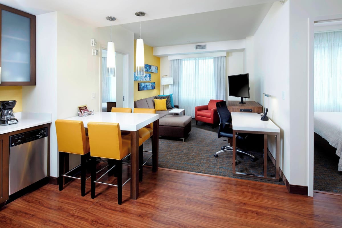 A hotel room with a dining area, a sofa, a TV, and a bed.