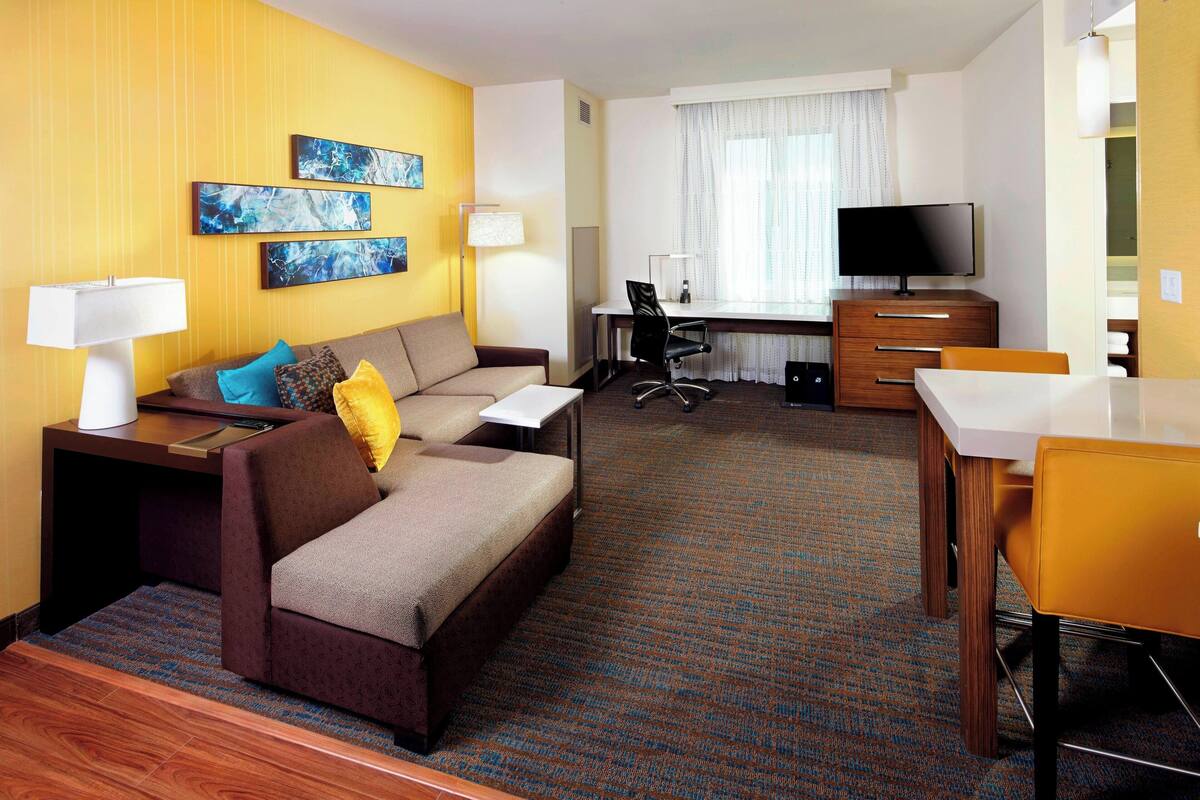 A hotel room with a sofa, a desk, a television, and a dining table.