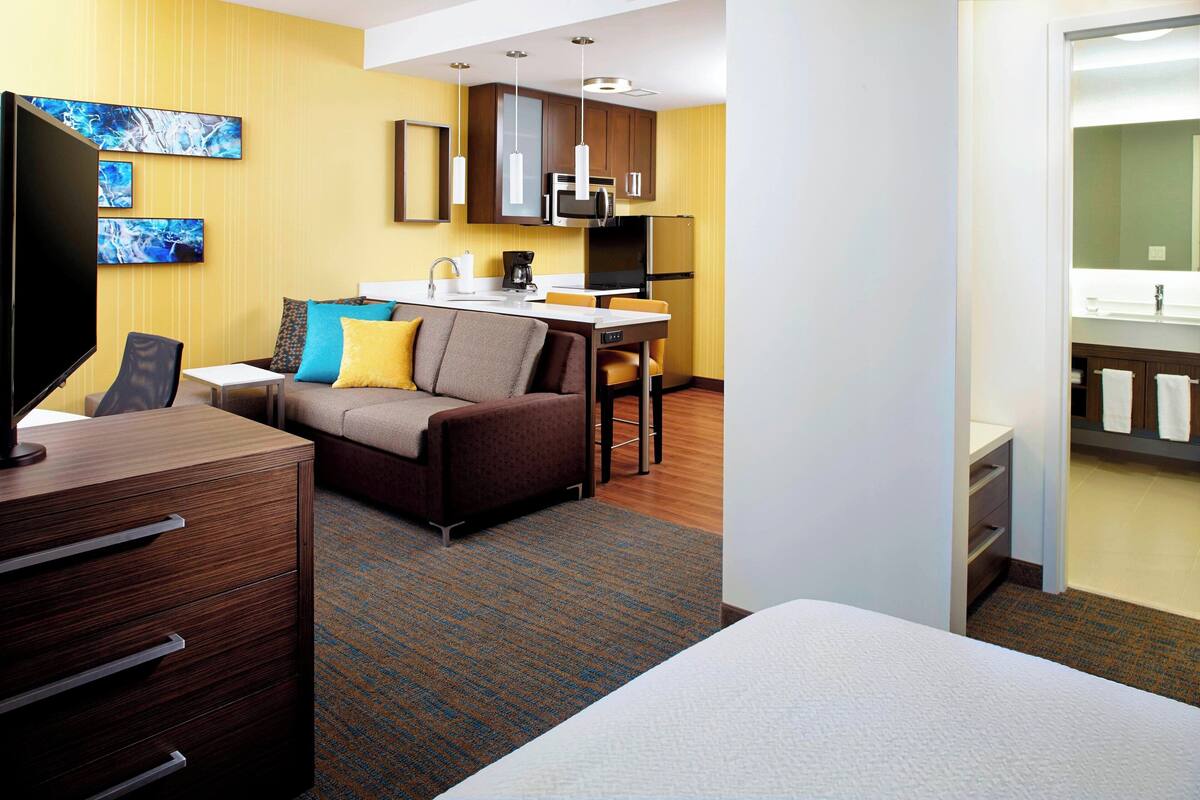 A hotel room with a bed, a desk, a sofa, a TV, and a kitchenette.