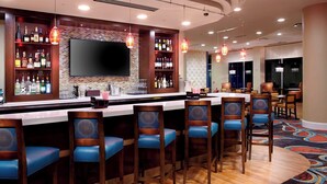 A bar area with multiple stools, a television mounted on the wall, and shelves stocked with bottles. - Residence Inn Secaucus Meadowlands (Secaucus)