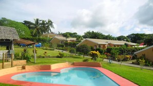 A swimming pool with a red border, surrounded by a well-maintained lawn and houses in the background. - Quest Apartments (Port Vila)
