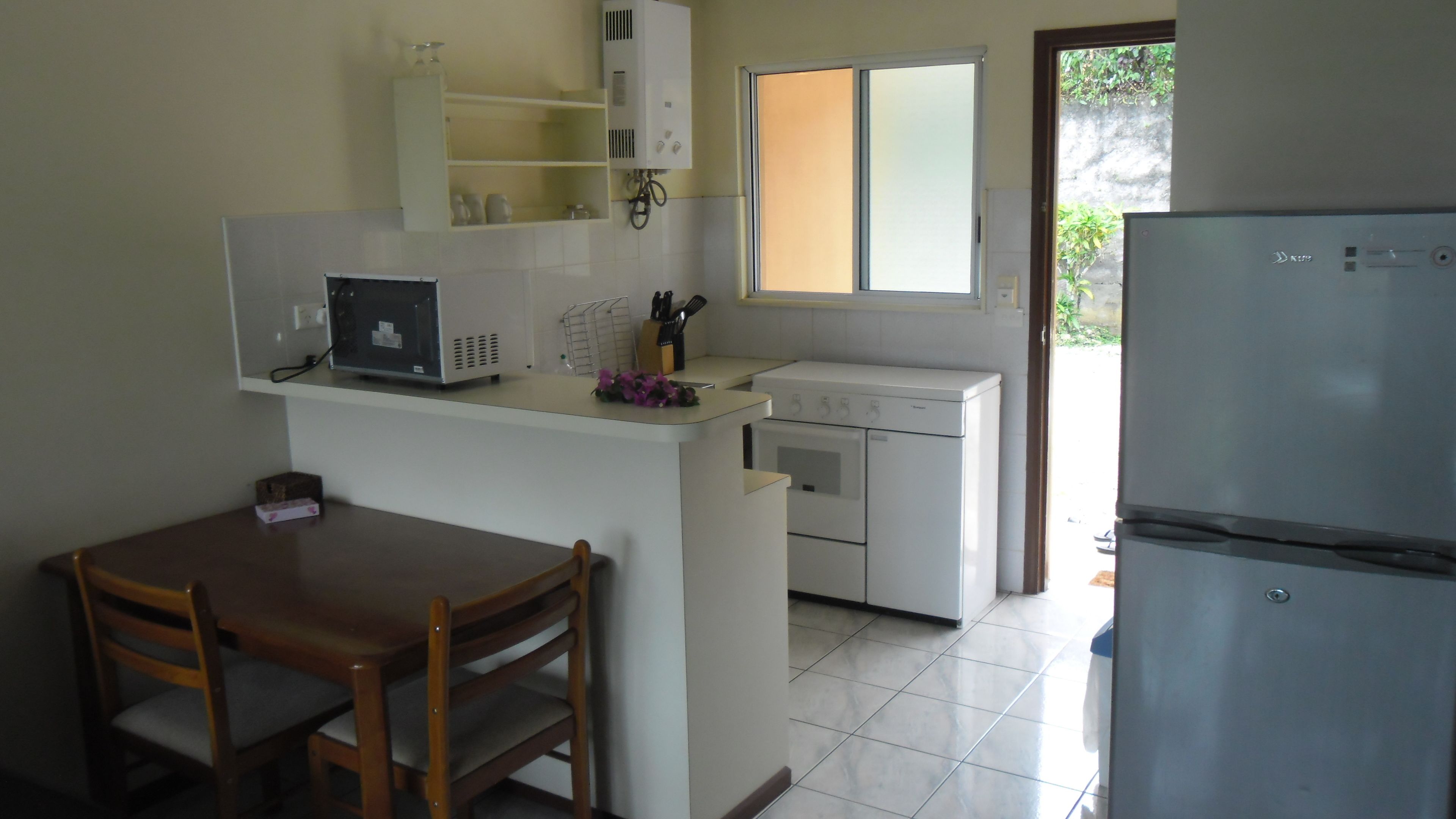 A compact kitchen with a refrigerator, a washing machine, and a small dining area with a table and chairs.