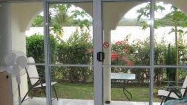 A room with a sliding glass door leading to a patio with a table and chairs, a fan, and greenery outside. - Quest Apartments (Port Vila)