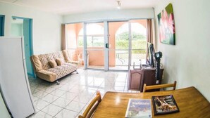 A room with a dining table, chairs, a sofa, and a sliding glass door leading to an outdoor area. - Quest Apartments (Port Vila)