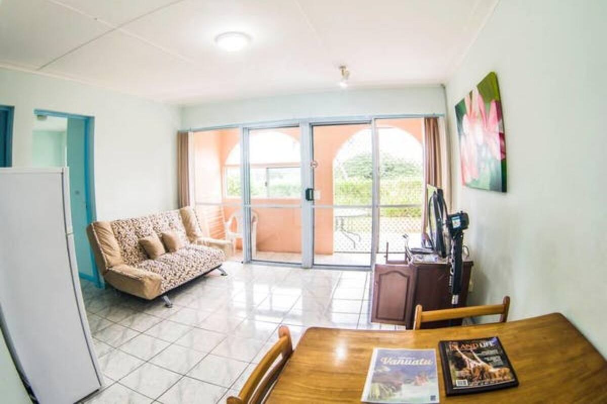 A room with a dining table, chairs, a sofa, and a sliding glass door leading to an outdoor area.