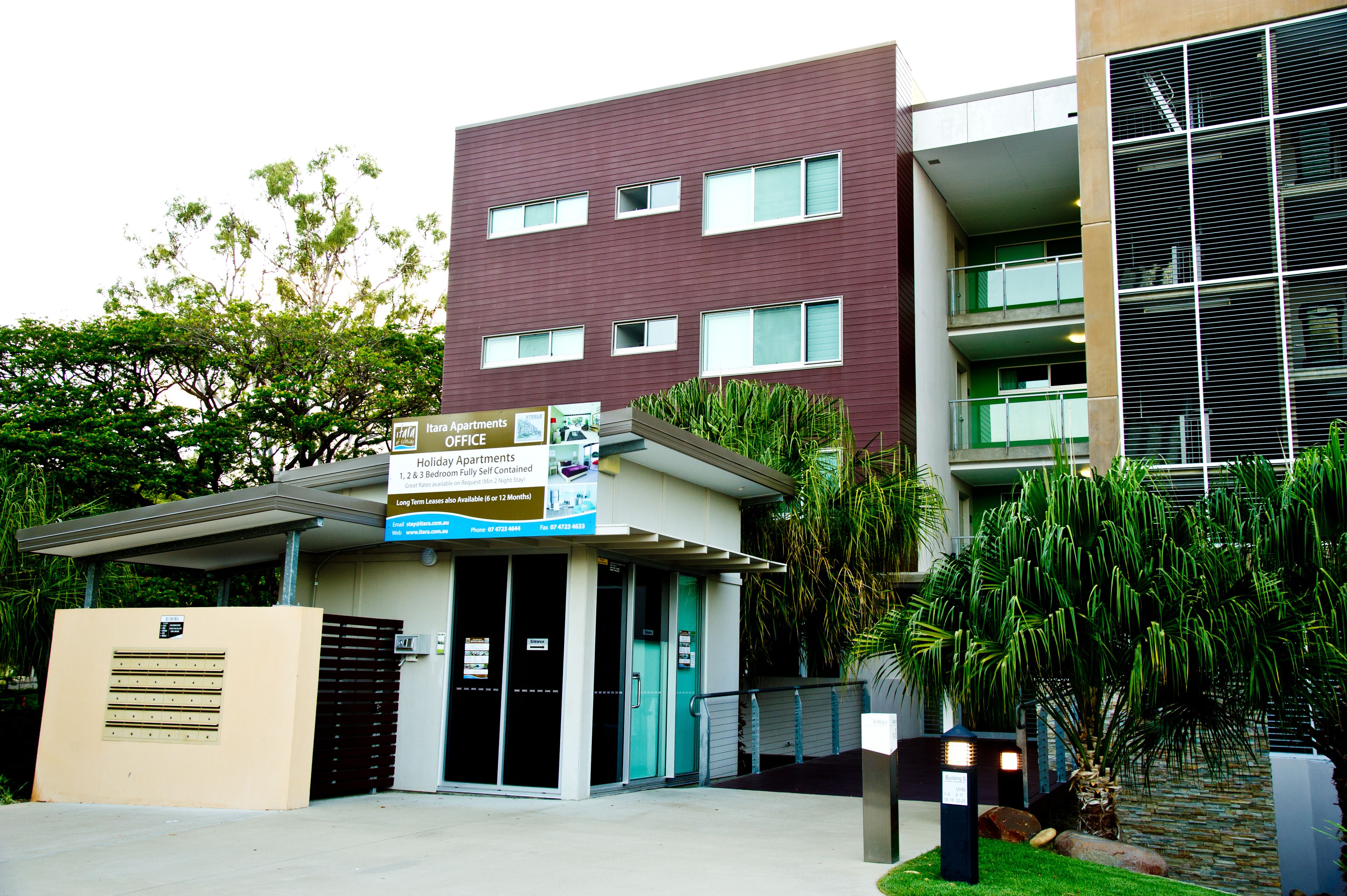 A modern building with multiple floors, a gated entrance, and a sign advertising holiday apartments.