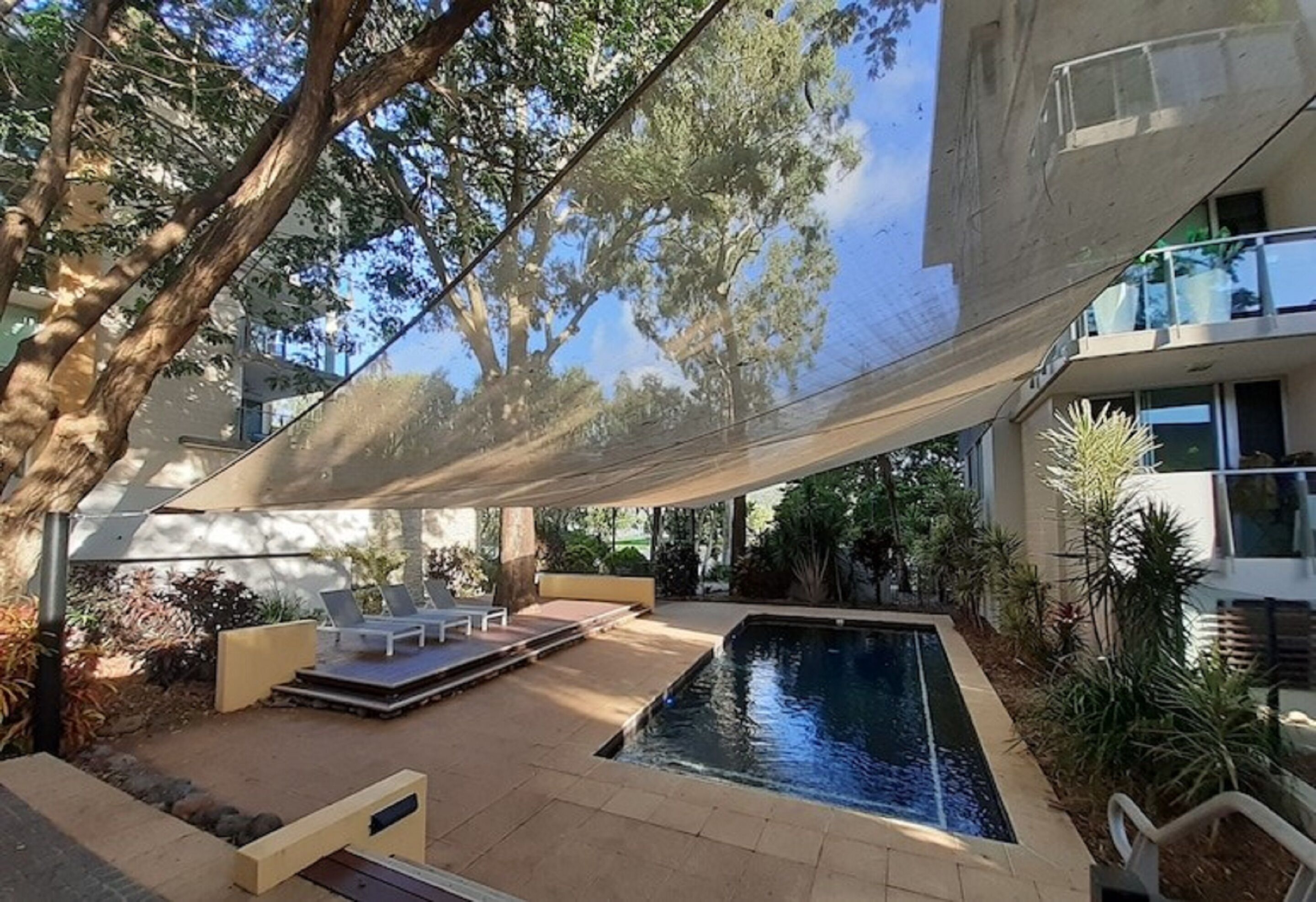 Et moderne poolområde med liggestole, en pool og en skyggefuld parasol.