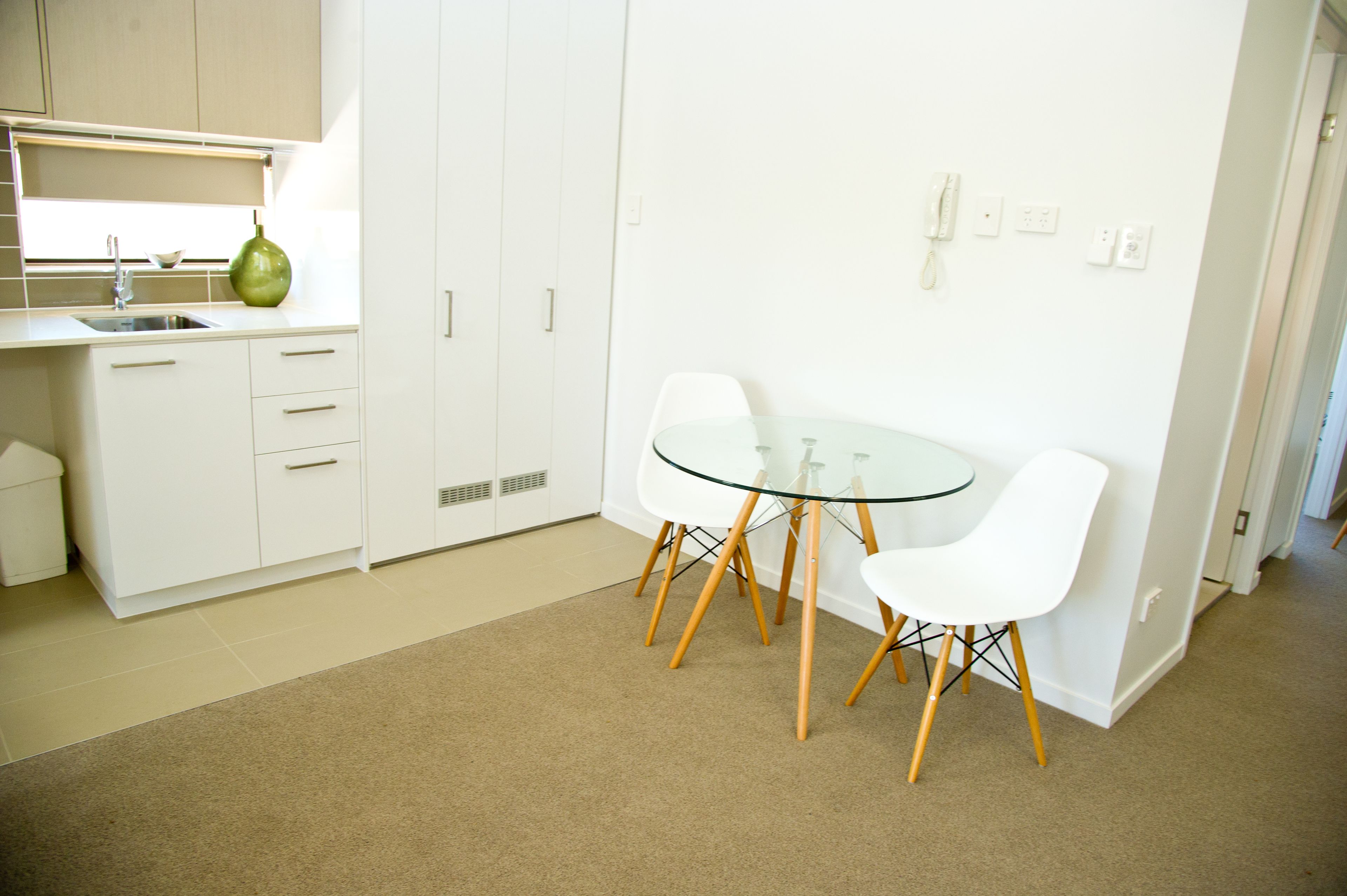 A modern kitchen with white cabinets, a glass table, and two white chairs.