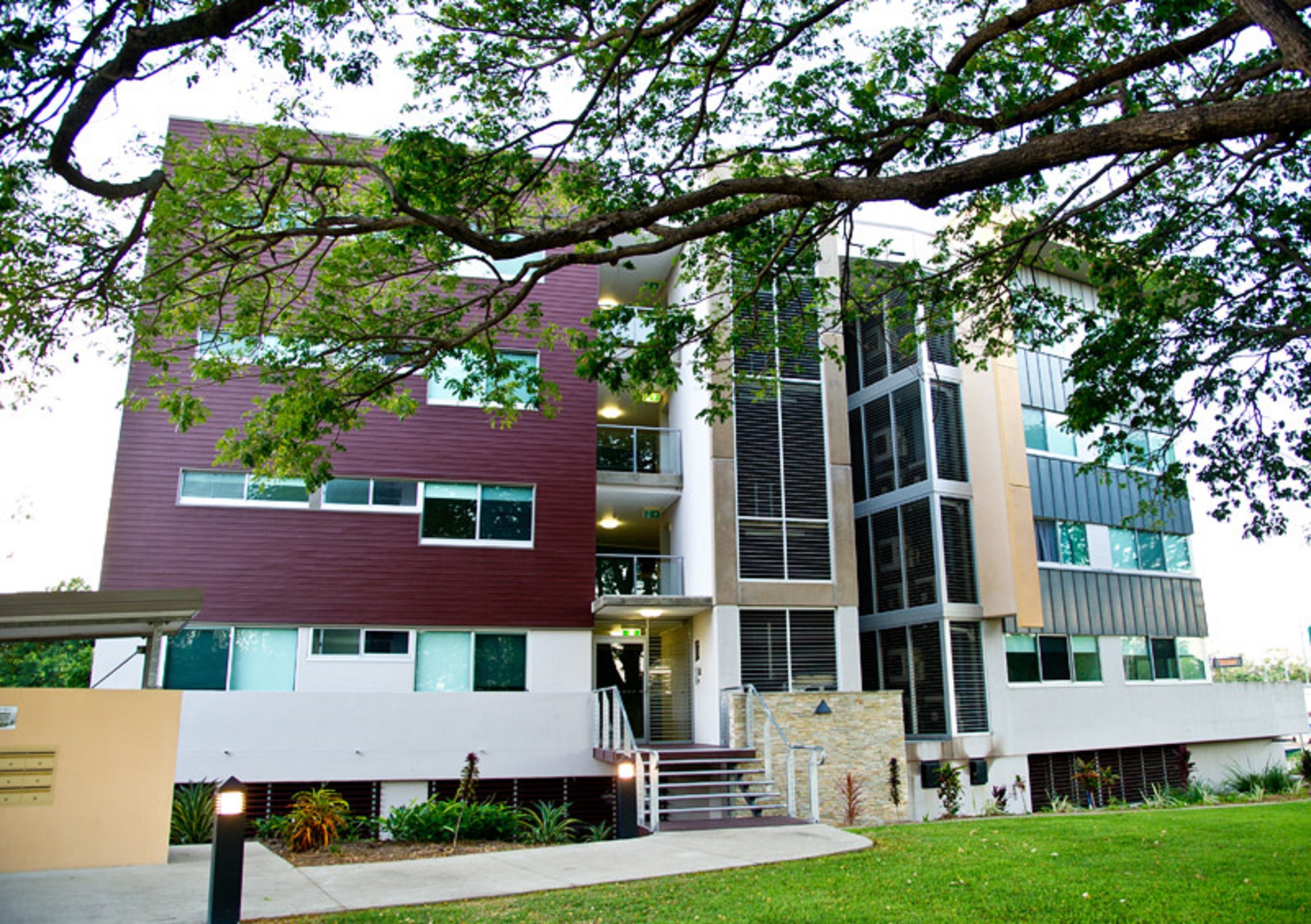 A multi-story building with a modern architectural design, featuring a combination of glass and solid panels, and a landscaped front yard with a pathway leading to the entrance.