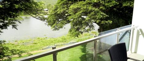 A balcony with a glass railing overlooking a lake and greenery.