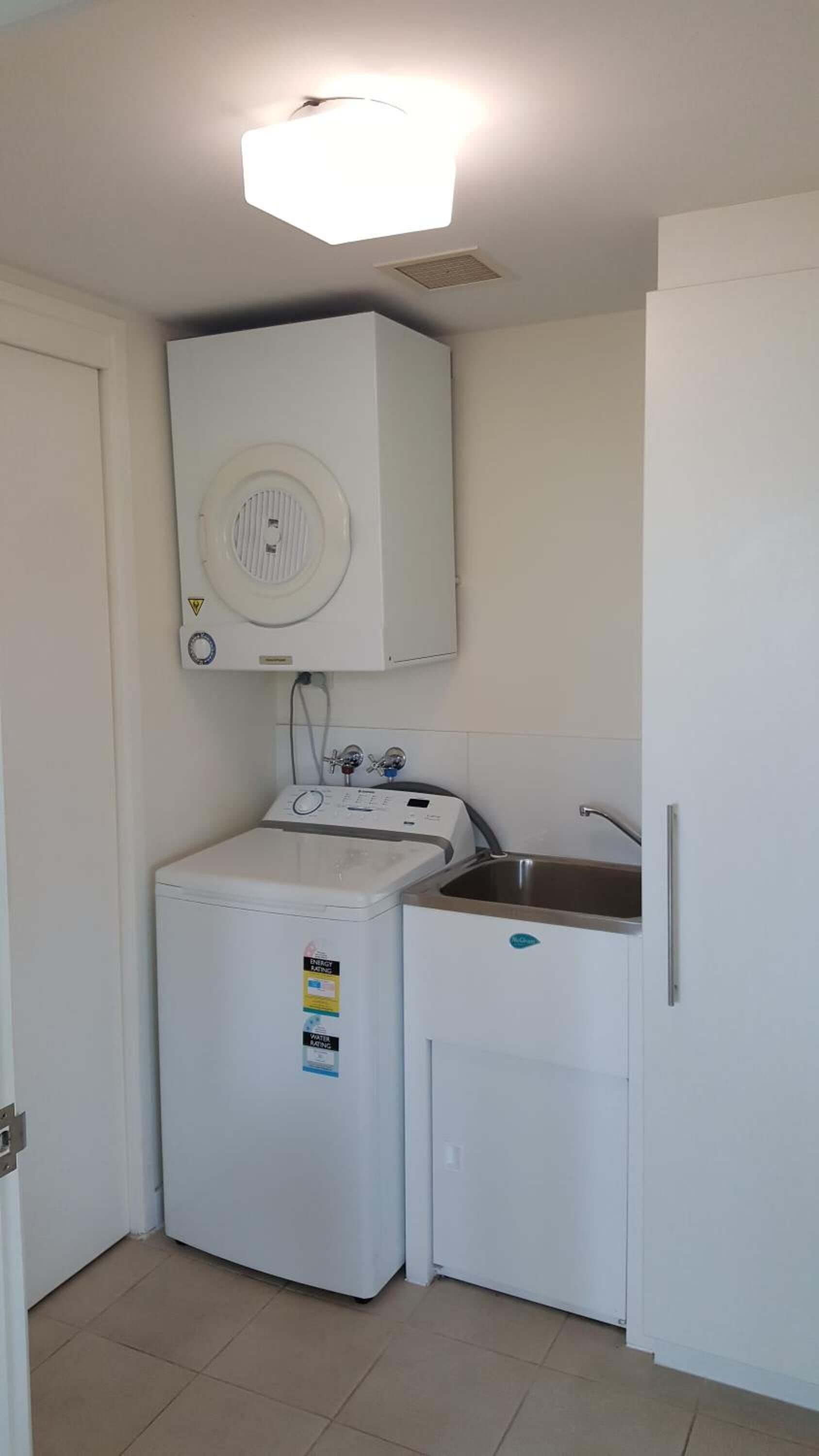 Une cuisine compacte équipée d’un lave-linge, d’un petit évier et d’un luminaire fixé au plafond.