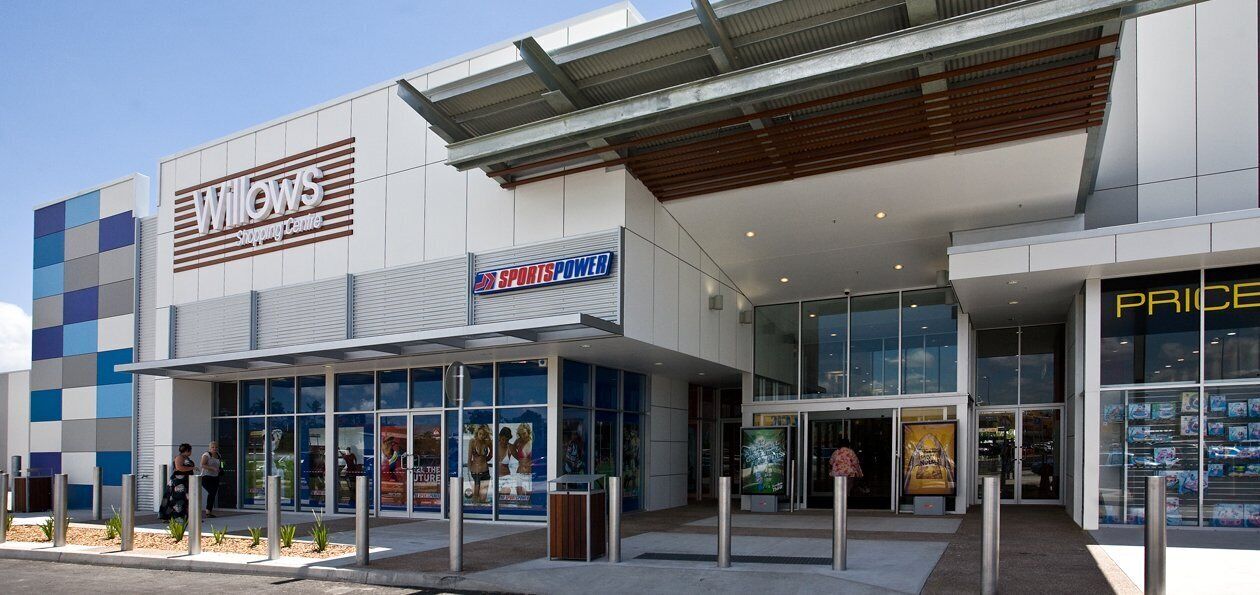 Ein modernes Gebäude mit Schildern 'Willows Shopping Centre', 'SportsPower' und 'Price', die auf ein Einzelhandelsgeschäft hinweisen.