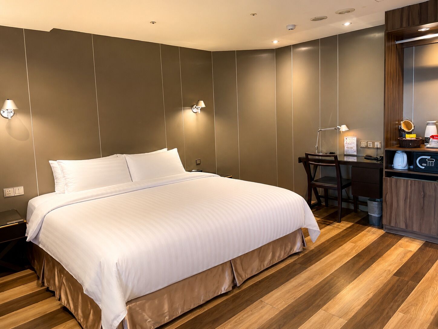 Habitación de hotel con una cama grande, un escritorio, una silla y una pequeña kitchenette.