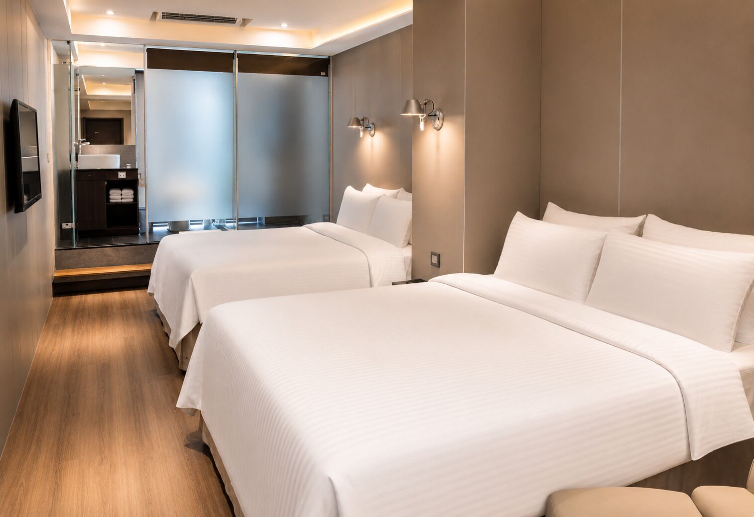 A hotel room with two beds, a bathroom, and a view of the hallway.