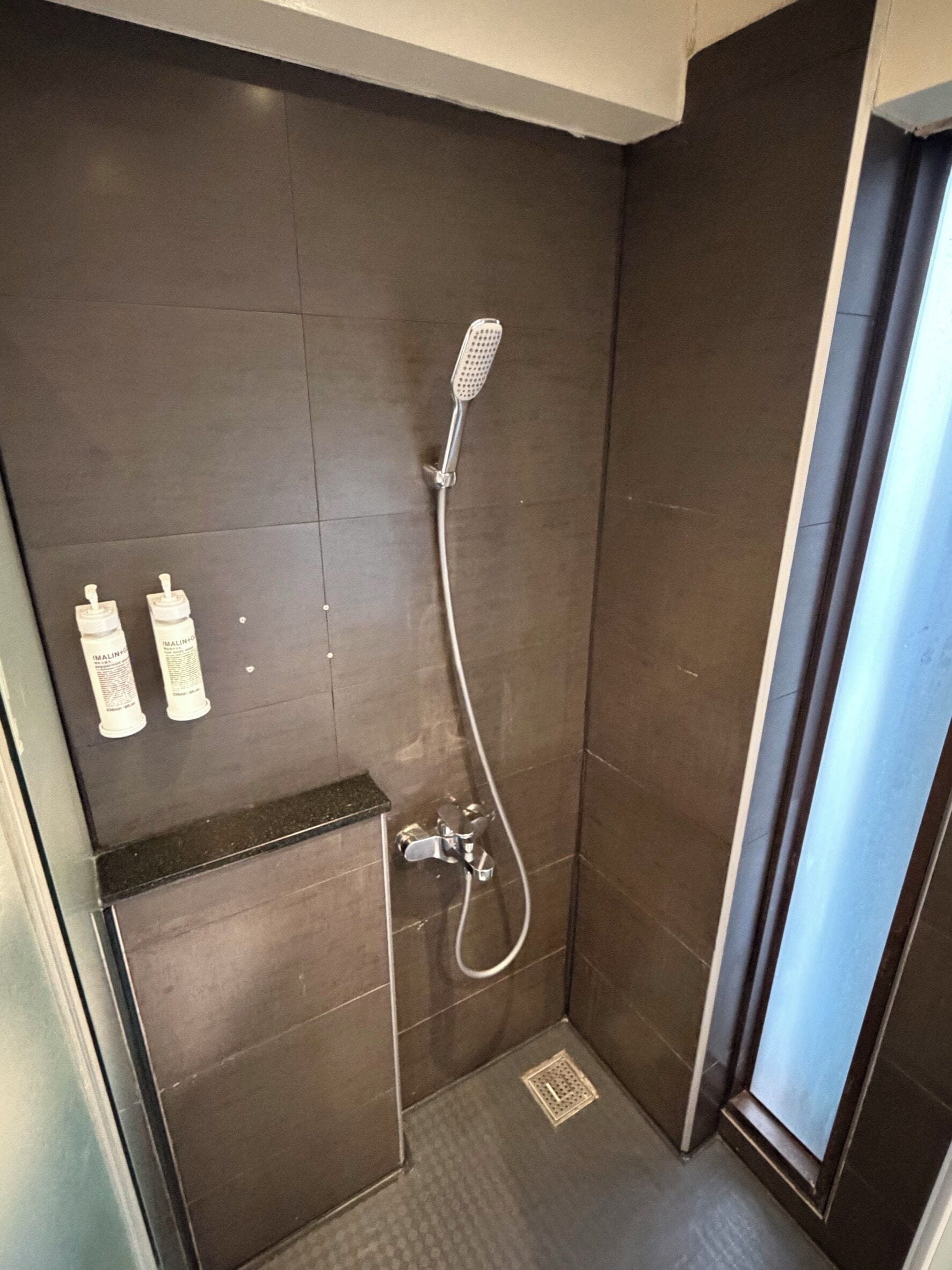 A shower with a handheld showerhead, a wall-mounted faucet, and two bottles of shampoo.