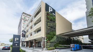 Un hotel de varios pisos con entrada de estacionamiento, un jardín vertical en la fachada y un paso peatonal superior.