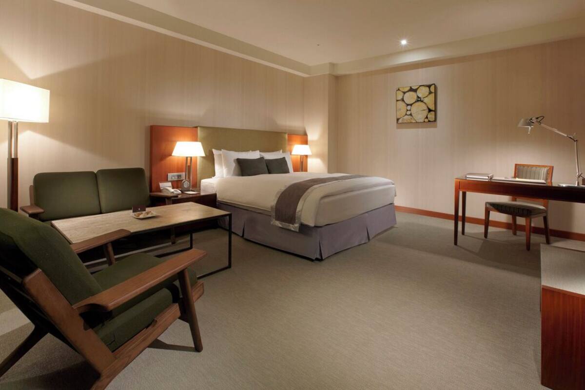 A hotel room with a bed, a desk, a chair, a sofa, and a lamp.
