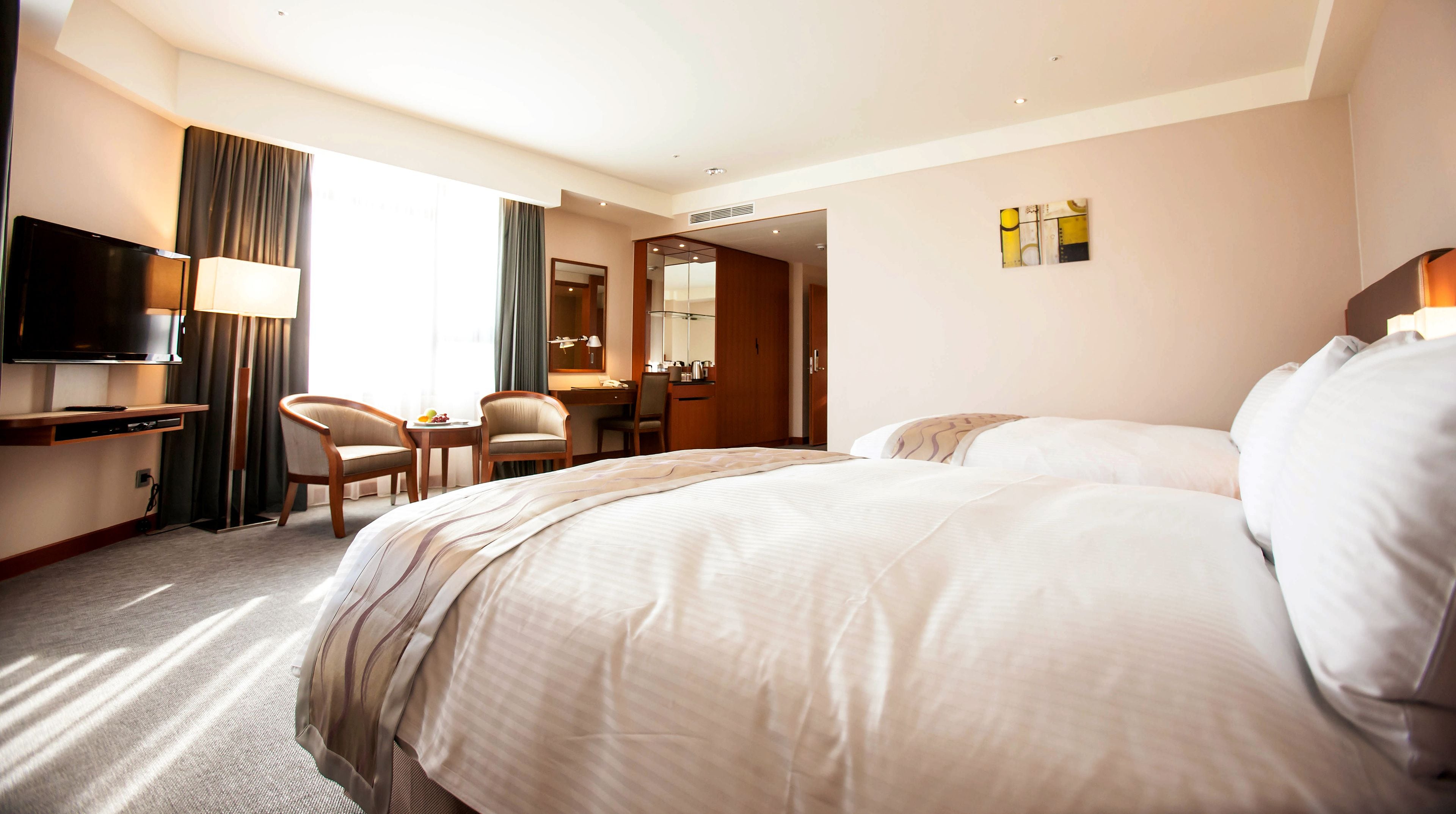 A hotel room with two beds, a desk, a chair, a TV, and a bathroom visible through an open door.