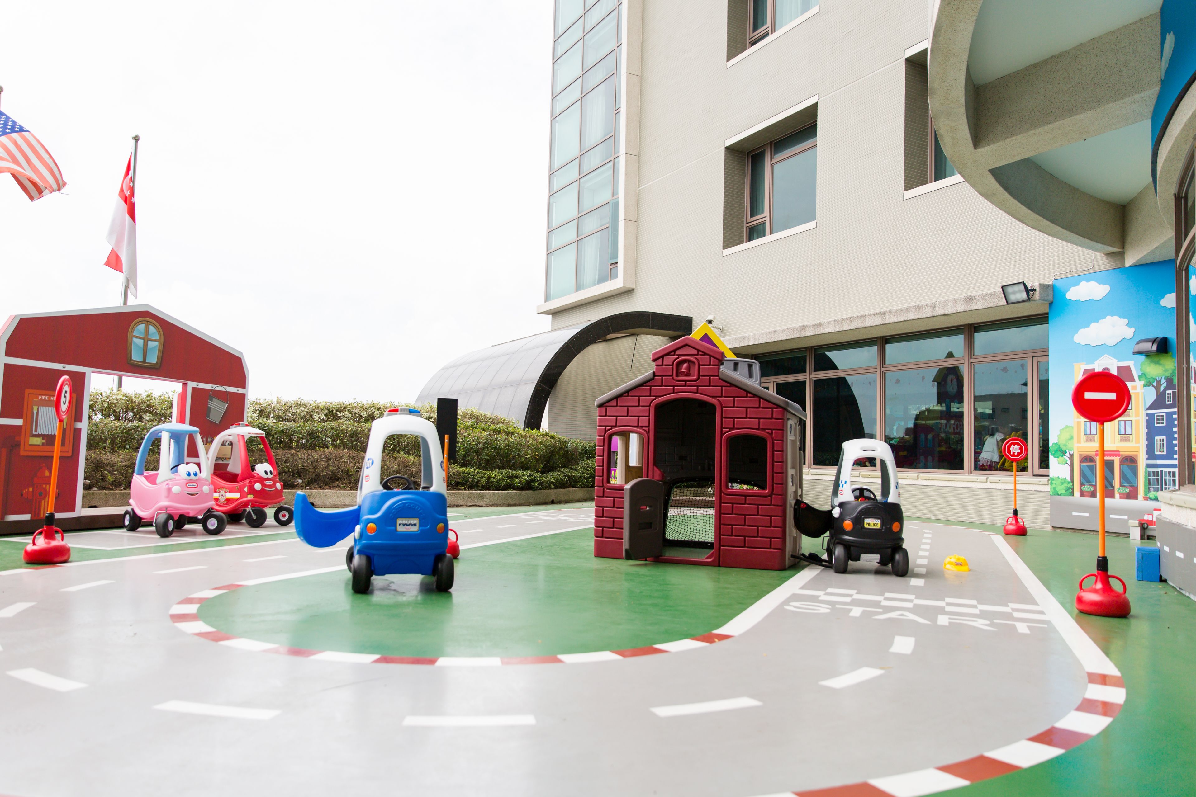 Zona de juegos infantiles con coches de juguete y un pequeño edificio de ladrillo.