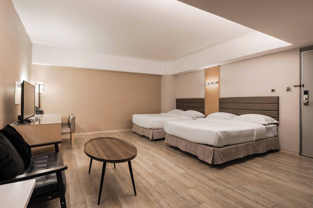 A hotel room with two beds, a desk, a chair, and a small table.