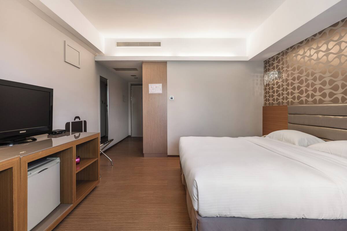 A hotel room with a bed, a TV, a mini-fridge, and a wooden dresser.
