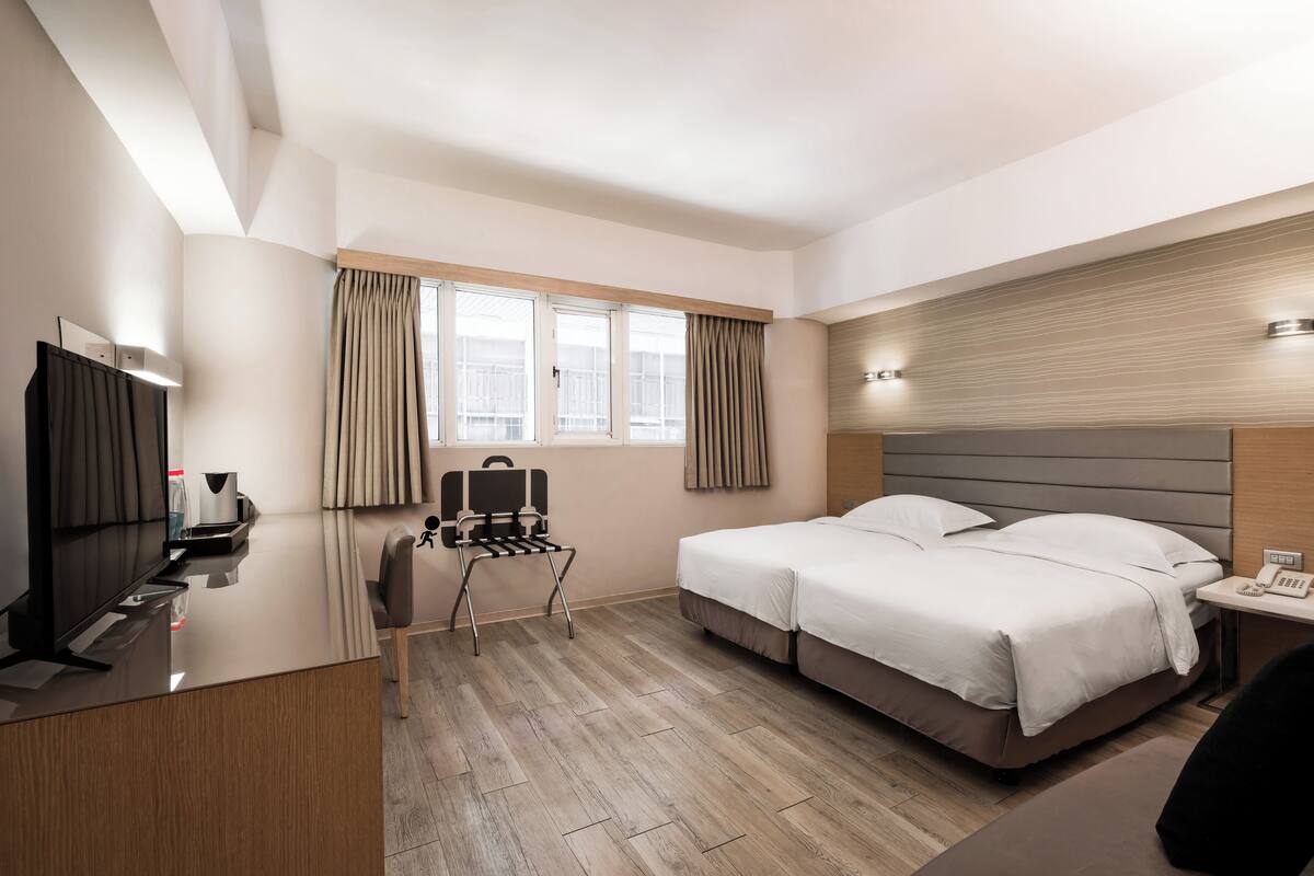 A hotel room with a bed, a desk, a chair, a TV, and a window with curtains.