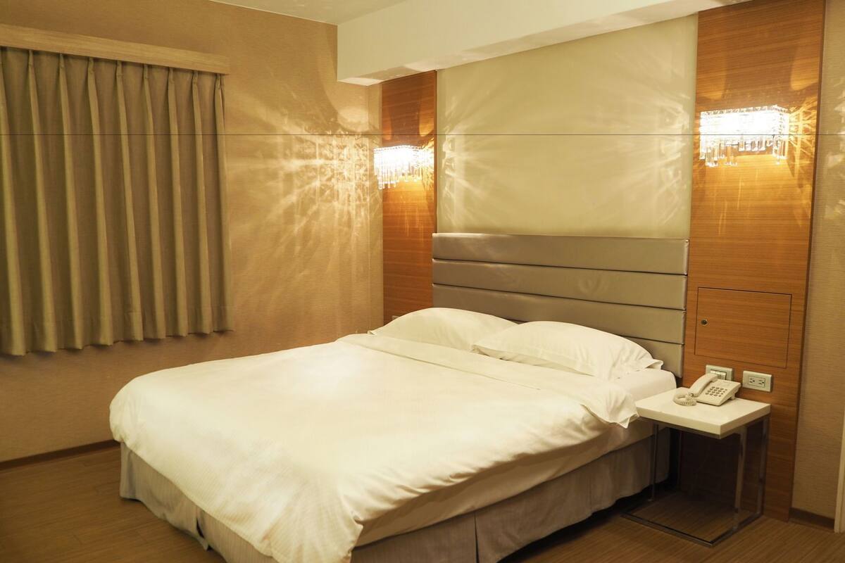 A hotel room with a large bed, a bedside table with a phone, and wall-mounted lighting.