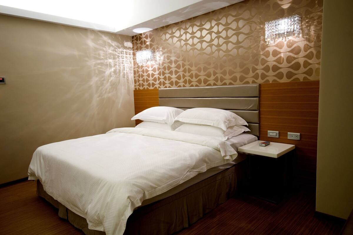 A hotel room with a bed, bedside table, and a patterned wall.