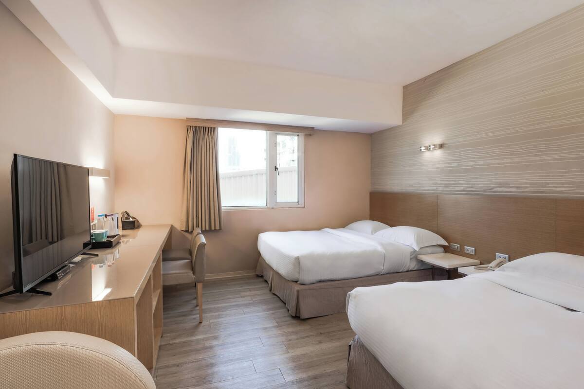 A hotel room with a bed, a desk, a television, and a window with curtains.
