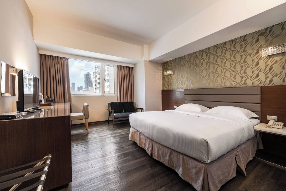 A hotel room with a large bed, a desk, a chair, and a television.