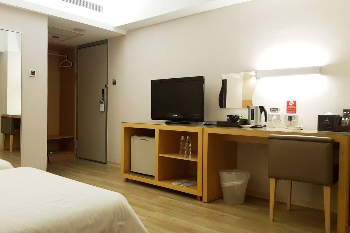 A hotel room with two beds, a TV, a desk with a computer, a mirror, and a wardrobe.