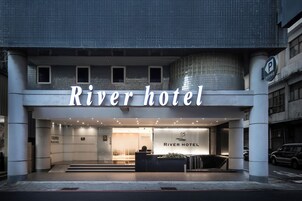 Exterior del Hotel River, con fachada moderna, mostrador de recepción y señal de estacionamiento.