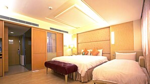 Une chambre d’hôtel avec un grand lit, un lit plus petit, un banc, une armoire et une salle de bain.