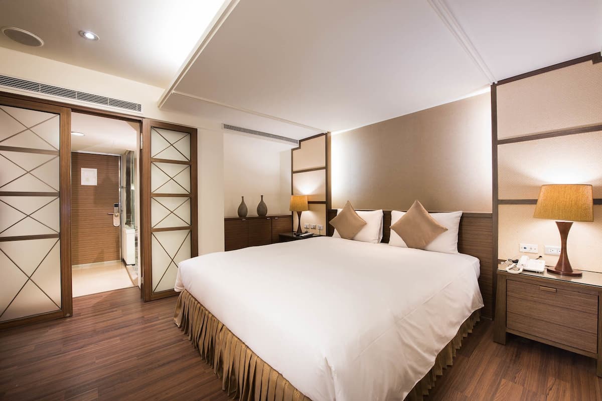 Una habitación de hotel con una cama grande, suelo de madera, una mesita de noche con lámpara y un armario con espejo.