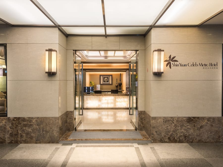 A hotel reception area with a modern design, featuring a reception desk, framed artwork, and a clear view into the hotel's interior.
