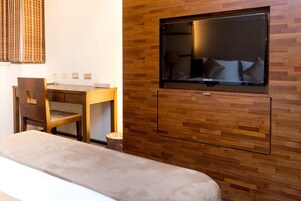 Una habitación de hotel con pared de madera, un televisor sobre la cama, un escritorio de madera y una silla.