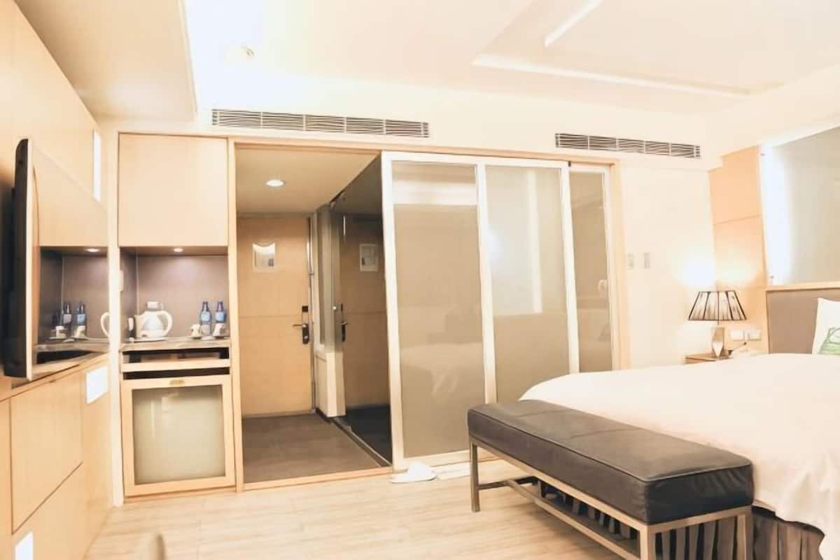 Una habitación de hotel con una cama, un banco, un televisor, un escritorio y un armario.