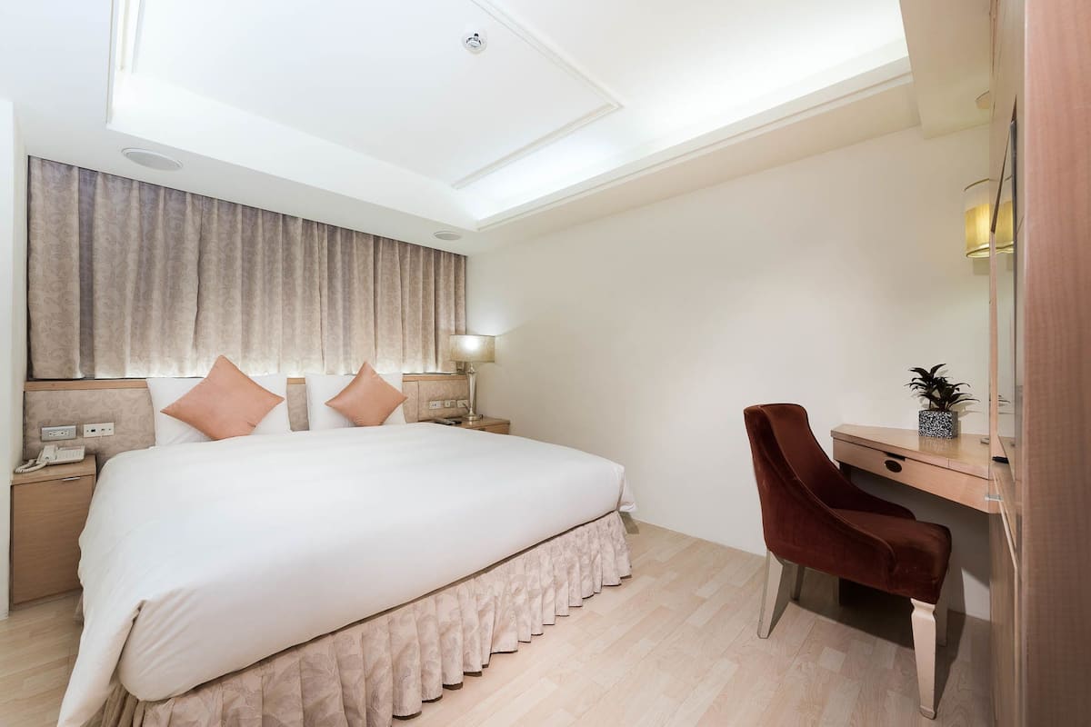 Habitación de hotel con una cama grande, un escritorio, una silla y una mesita de noche con lámpara.