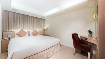A hotel room with a large bed, a desk, a chair, and a nightstand with a lamp.