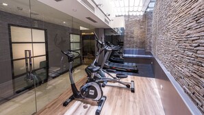 Une salle de sport équipée de tapis de course, de vélos d’exercice et d’un mur en pierre.