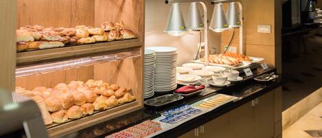 A buffet counter with various baked goods, plates, and condiments.