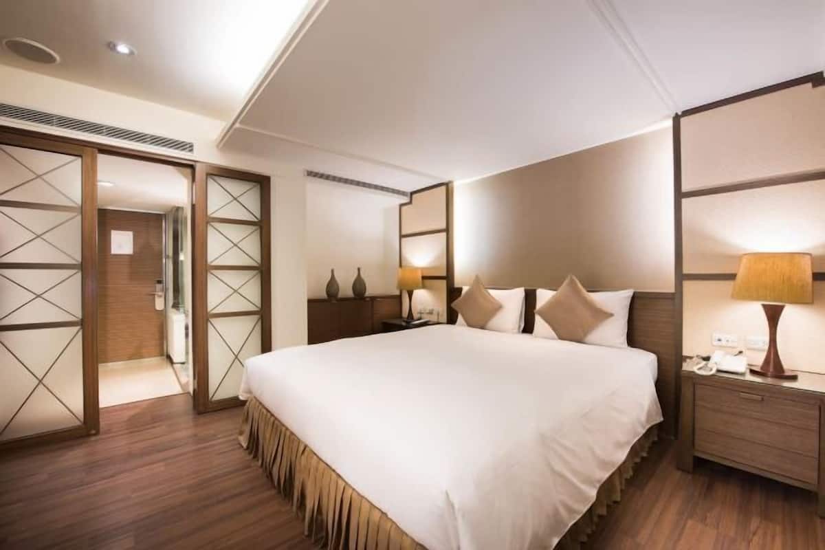 Una habitación de hotel con una cama grande, mesitas de noche, un armario y un espejo.