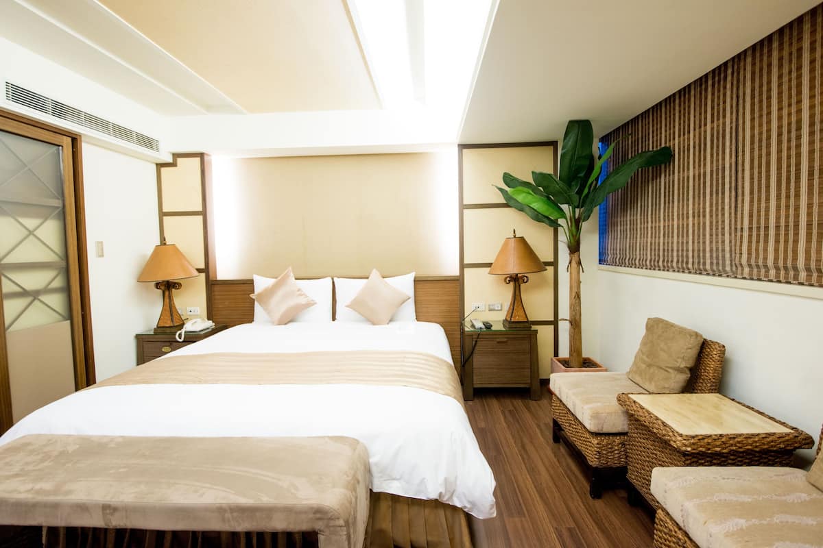 Habitación de hotel con una cama grande, dos mesitas de noche con lámparas, un sofá pequeño y una planta en maceta.
