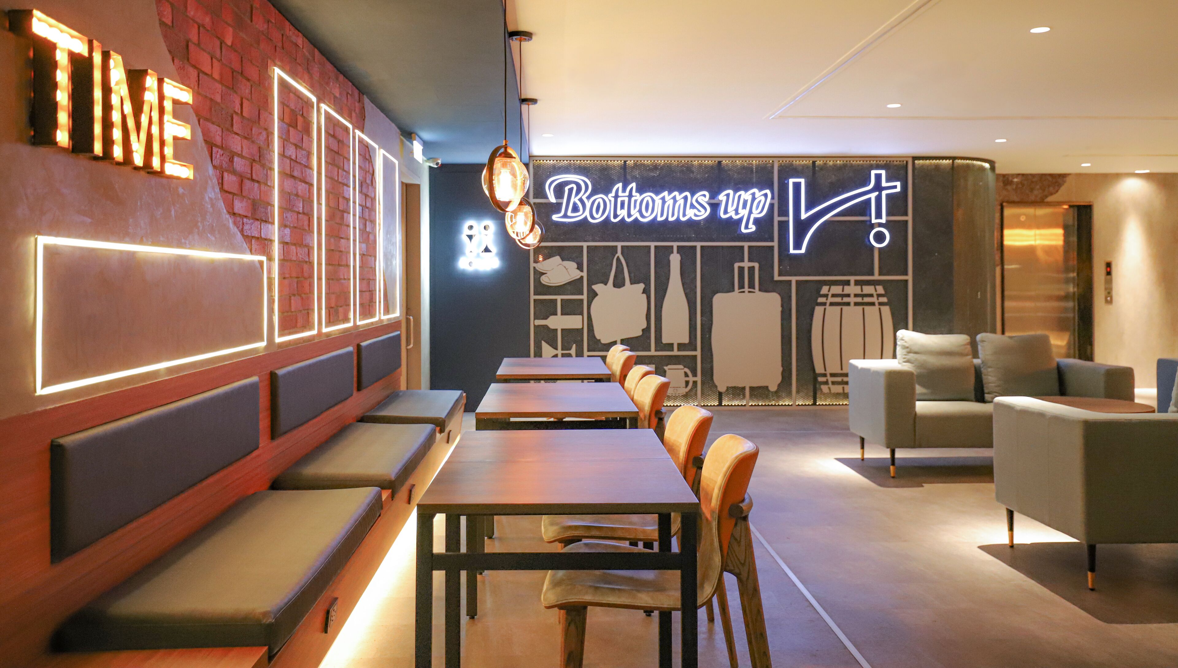 A restaurant interior with wooden tables and benches, a neon sign reading "Bottoms up!", and a brick wall with illuminated letters.