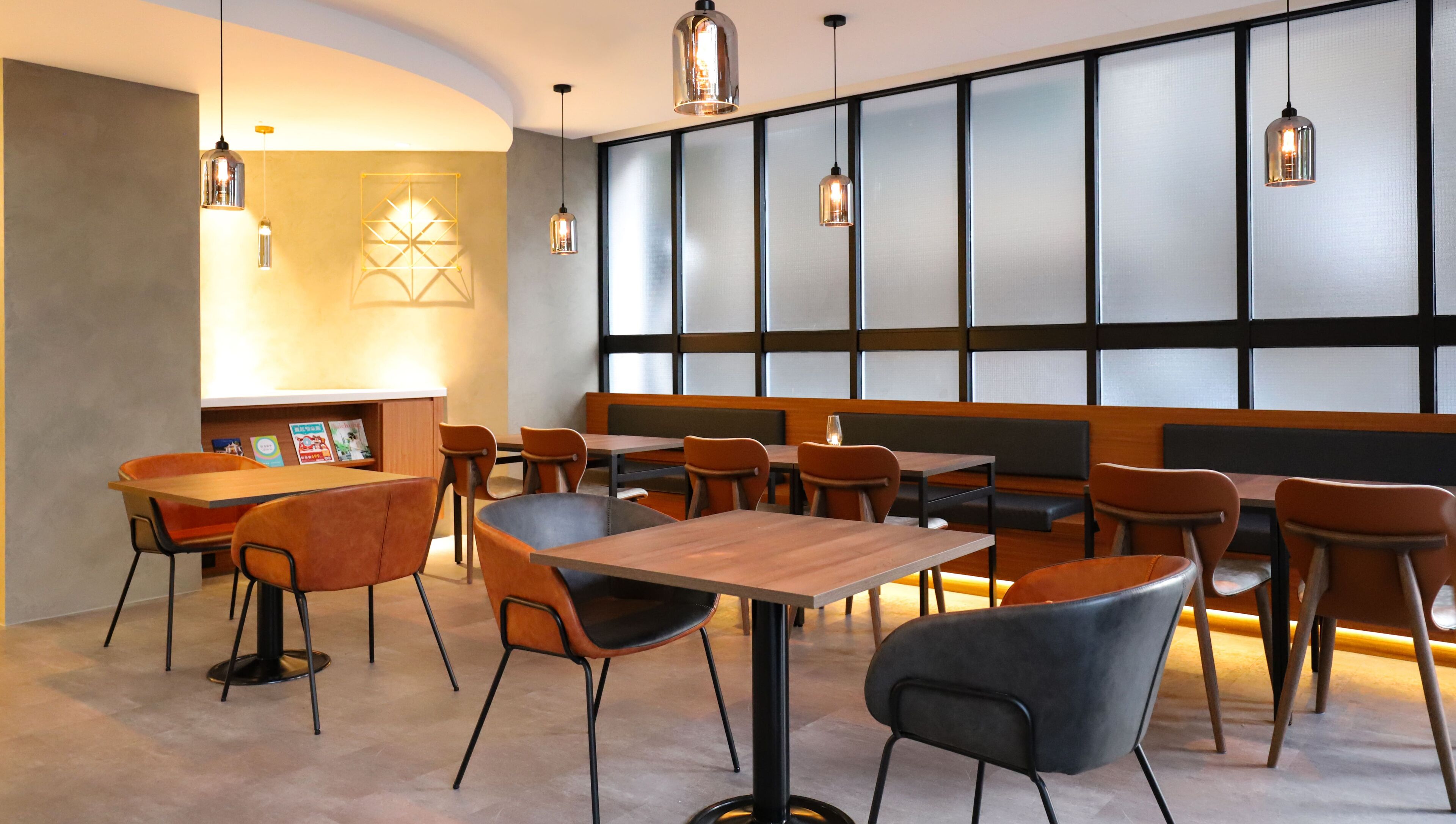 A modern restaurant with wooden tables and chairs, a seating area with cushions, and pendant lighting.