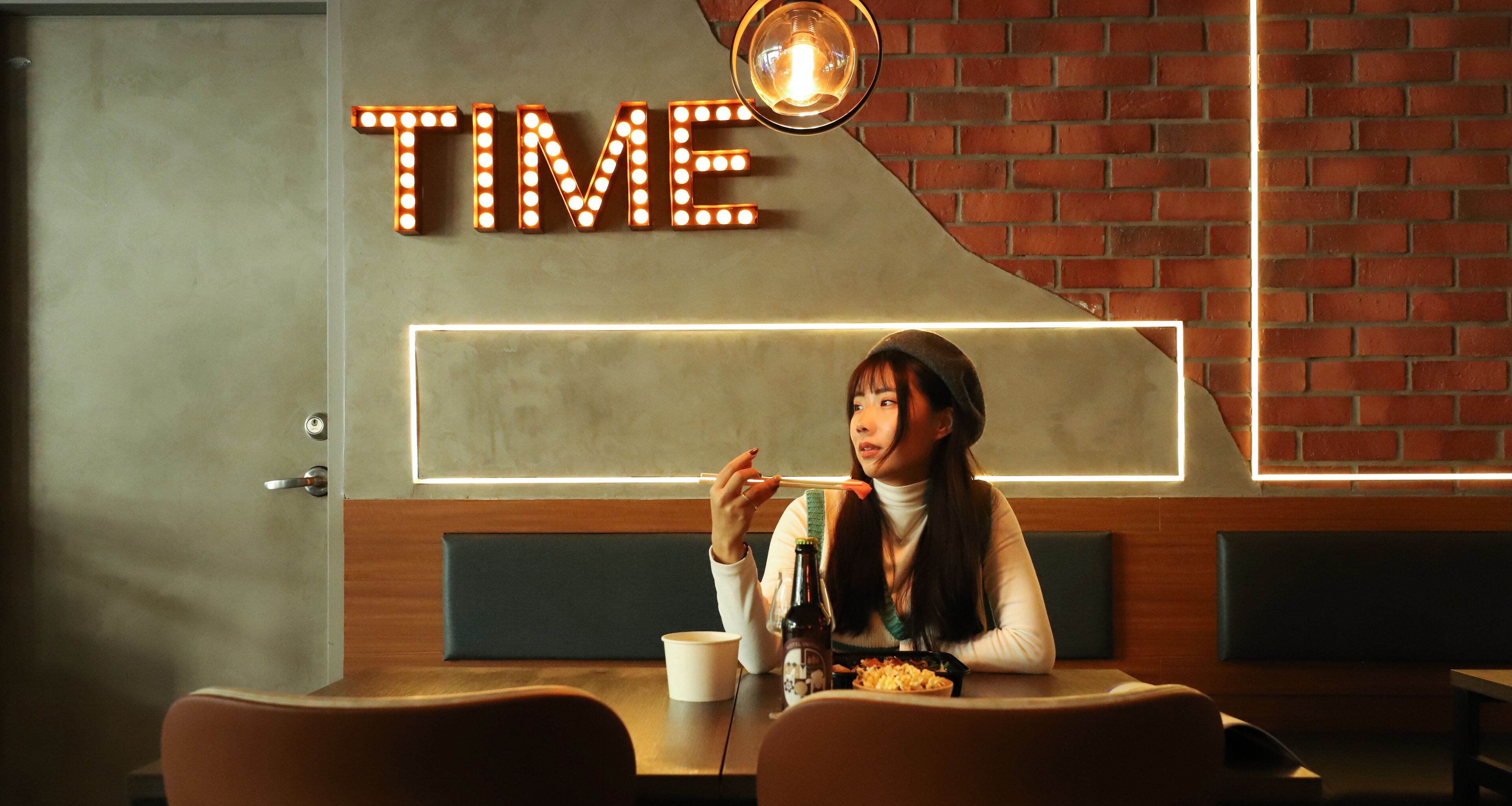 A person sitting at a table in a restaurant with a neon sign on the wall that reads "TIME".