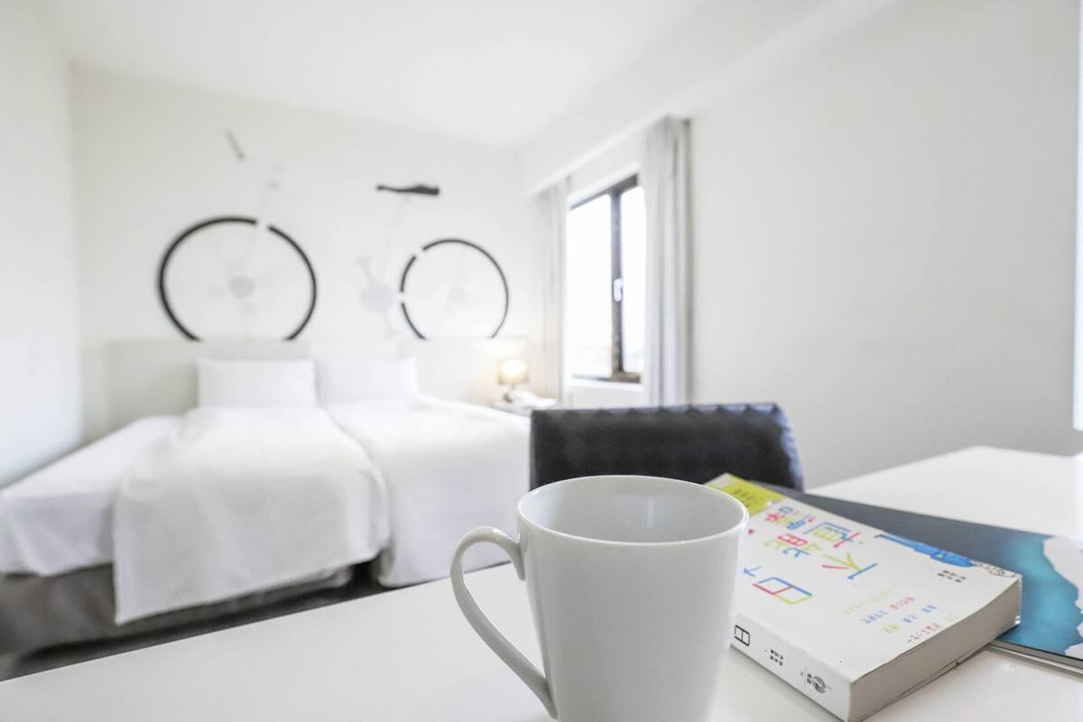 Een hotelkamer met een bed, een nachtkastje met een mok, een stoel en een raam.