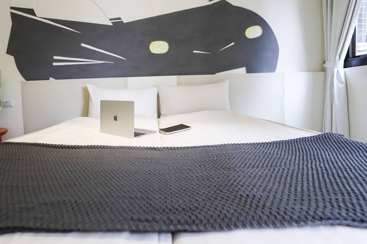 Een opgemaakt bed met een laptop en notitieboek, een lamp en een kat in de wanddecoratie.