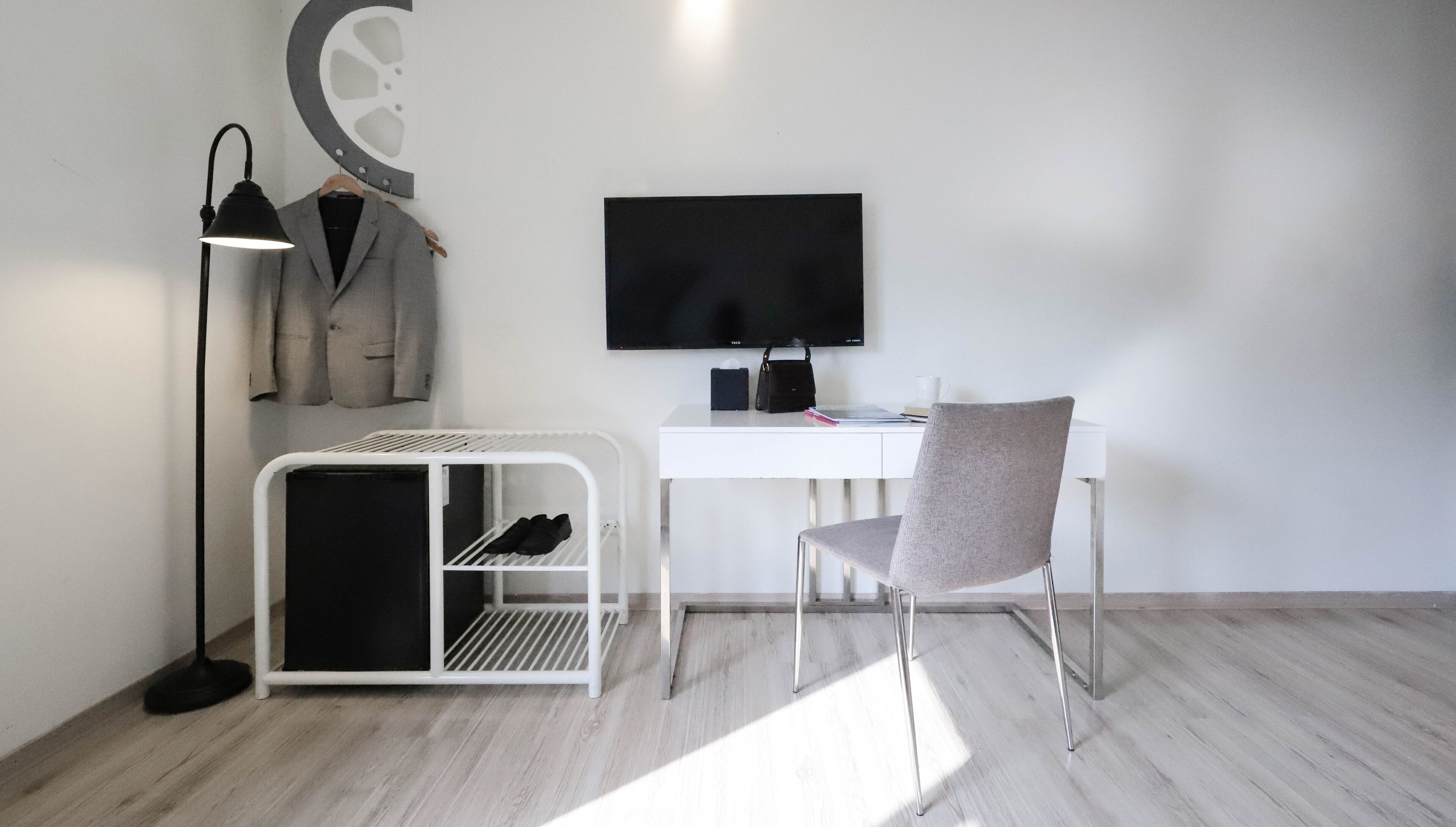A modern office space with a desk, chair, and a coat rack with suits.
